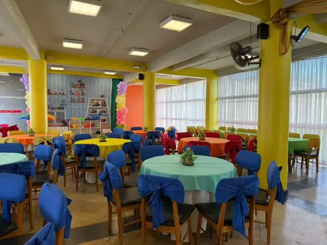 Salón con mesas de manteles celestes y sillas vestidas, aire acondicionado y ventanales
